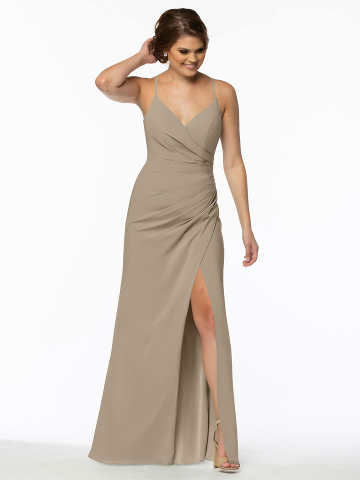 A woman models the Avery Austin 80114: a sleeveless taupe chiffon bridesmaid dress with V-neck, ruched waist, and high slit. She smiles against a white background, wearing strappy heels and touching her hair.
