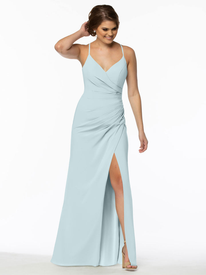A woman stands smiling with one hand in her hair, wearing Avery Austin’s TH-80114 sky blue chiffon bridesmaid dress featuring spaghetti straps, a V-neckline, ruched waist, and thigh-high slit with high-heeled sandals.