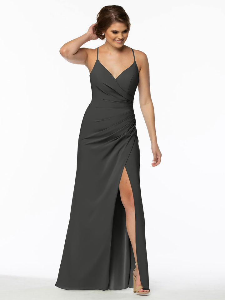A woman stands against a white background, smiling and touching her hair, wearing the Avery Austin TH-80114 sleeveless ruched bridesmaid dress in steel gray with thin straps, a V-neckline, and a thigh-high slit.