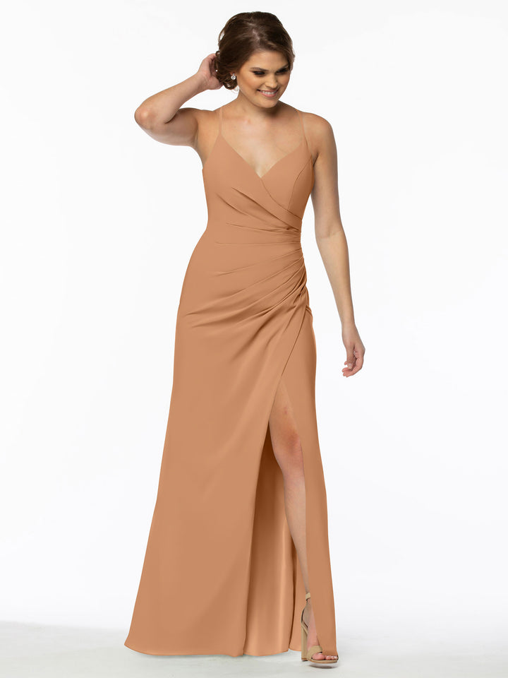 A woman stands smiling with one hand in her hair, wearing Avery Austin’s sleeveless chiffon bridesmaid dress 80114. The light brown gown features a v-neckline, high slit, and is paired with chic high-heeled sandals.