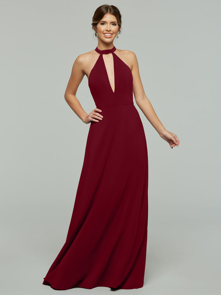 A woman wearing Avery Austin’s 80115, a sleeveless floor-length burgundy halter A-line dress with a keyhole cutout, stands against a light gray background, smiling with one hand on her hip.