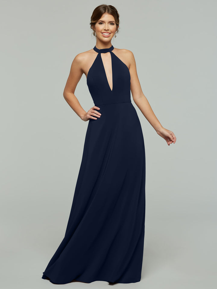 A woman is smiling, standing against a plain gray background wearing the Avery Austin 80115, a sleeveless, floor-length navy blue halter A-line dress with a front keyhole cutout.