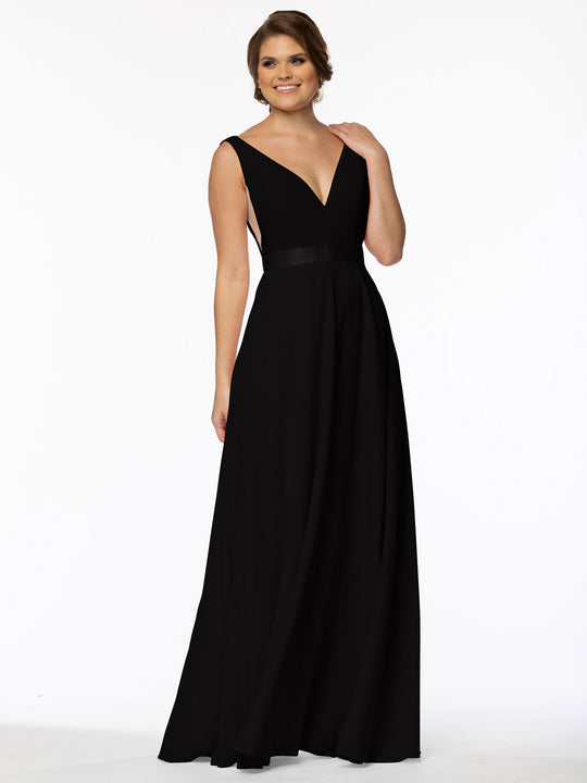 A woman poses happily in Avery Austin’s 80117—a sleeveless, floor-length black gown with a deep V-neck, fitted waist, illusion plunge sides, and an elegant A-line silhouette—set against a plain white background.