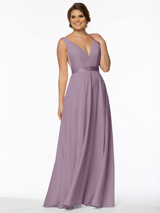 A woman smiles against a white background wearing Avery Austin style 80117, a sleeveless lavender gown with a deep V-neck, illusion sides, and fitted waist.