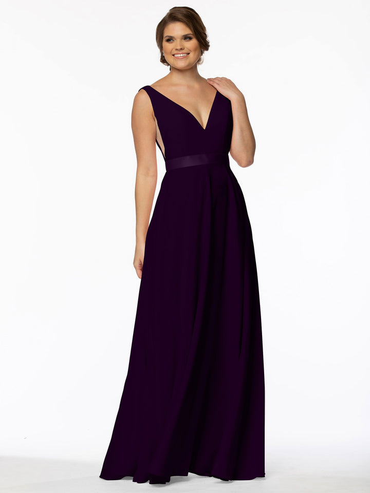 A woman smiles against a white background, touching her shoulder while wearing Avery Austin&