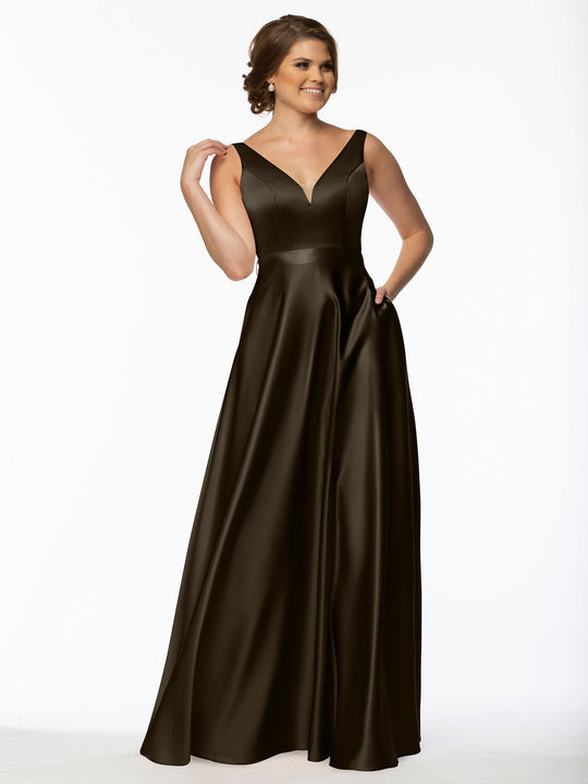 A woman in Avery Austin’s 80118— a sleeveless, floor-length dark brown satin bridesmaid dress with V-neck, fitted bodice, full skirt, and pockets—smiles with one hand on her hip and the other touching her hair.