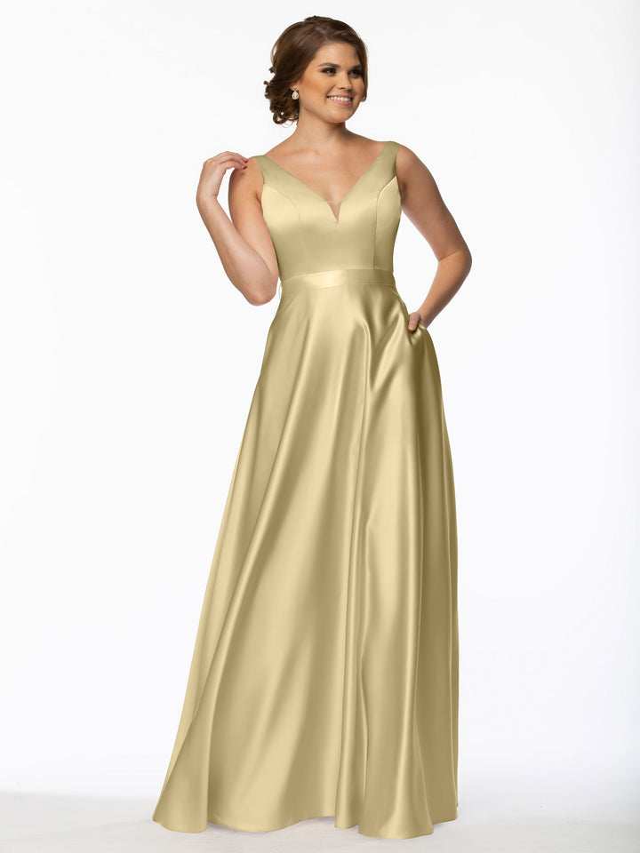A woman smiles in the Avery Austin 80118, a floor-length gold satin bridesmaid dress featuring a V-neckline, fitted bodice, and full skirt. One hand rests on her hip while the other touches her hair, highlighting this elegant style.