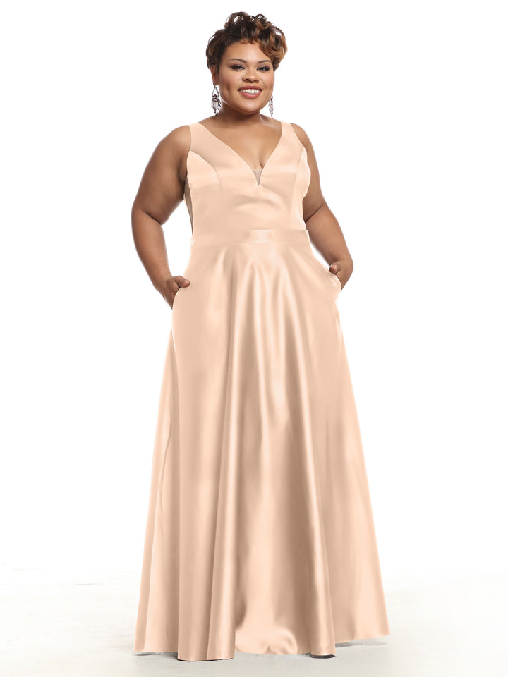 A woman smiles against a white background wearing the Avery Austin 80118 sleeveless satin bridesmaid dress with a deep V-neckline, floor-length hem, pockets, and a light peach color.