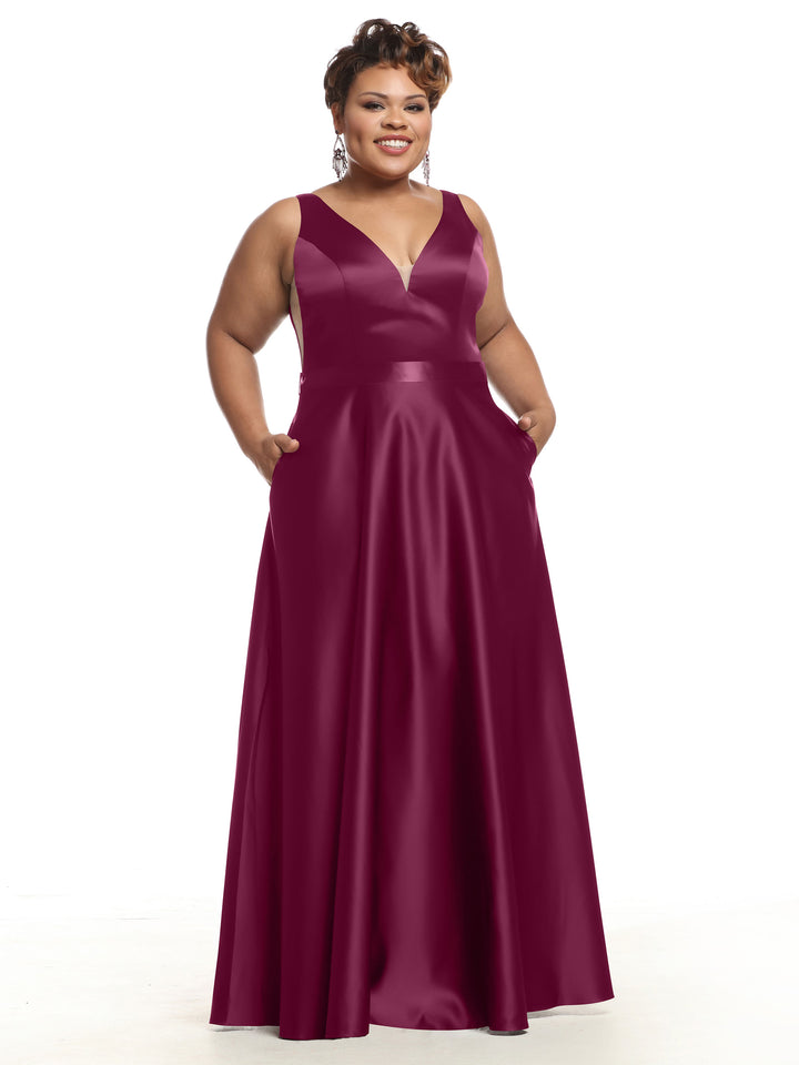 A woman wearing Avery Austin’s 80118 sleeveless deep burgundy satin bridesmaid dress with a V-neckline and pockets, smiling against a white background.
