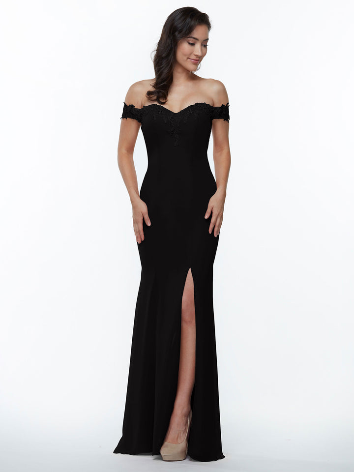 A woman wears Avery Austin style 80121, an off-the-shoulder black bridesmaid dress with a thigh-high slit and lace accents, paired with nude heels. She stands smiling against a plain white background with her hands at her sides.