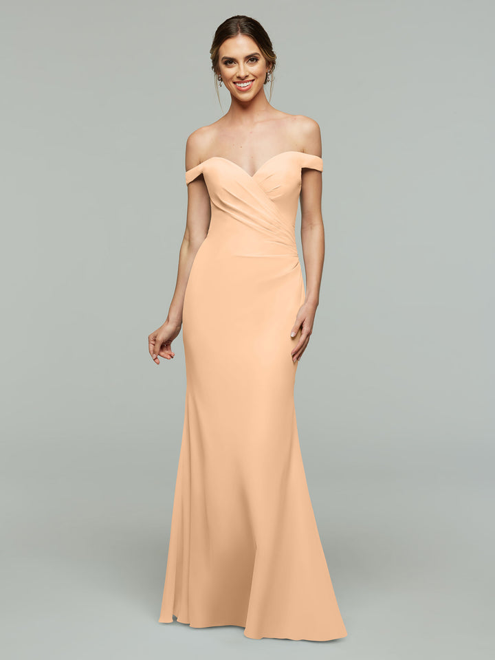 A woman in a blush off-the-shoulder bridesmaid dress (Avery Austin 80122) smiles against a plain gray background.
