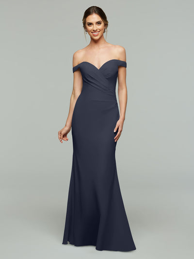 A woman smiles against a light gray background wearing Avery Austin’s 80122, a dark navy blue, off-the-shoulder bridesmaid dress. The floor-length gown has a fitted bodice and a gently flared hem for an elegant look.