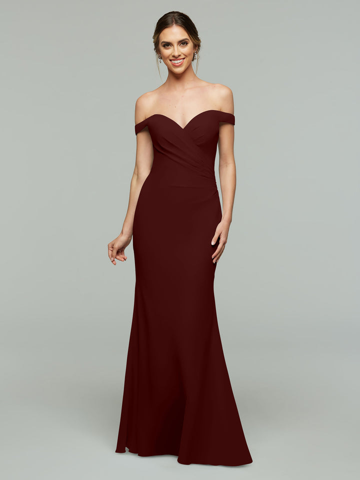 A woman in the Avery Austin 80122 off-the-shoulder, floor-length bridesmaid dress in Merlot smiles against a plain light gray background.