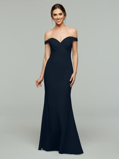 A woman smiles in Avery Austin’s 80122, an elegant off-the-shoulder navy blue bridesmaid gown with a fitted bodice and slight flare hem, posing against a plain light gray background.