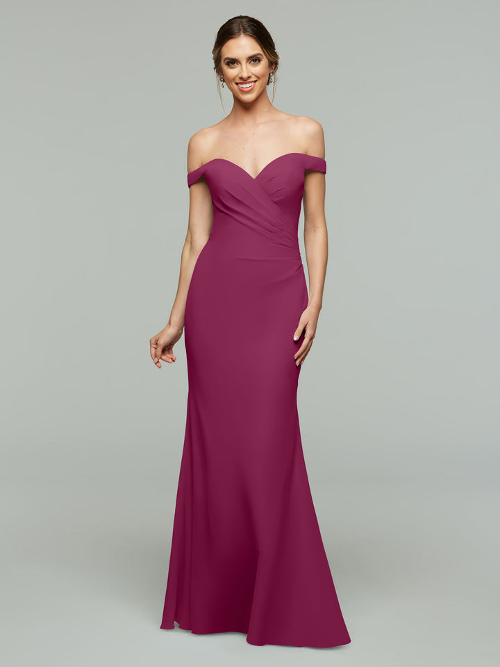 A woman in Avery Austin’s 80122 off-the-shoulder magenta chiffon gown stands against a light gray background, smiling with her hair in a chic updo. The ruched, floor-length bridesmaid dress exudes elegant, timeless style.