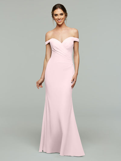 Wearing Avery Austin style 80122, a woman stands smiling against a plain gray background in a light pink off-the-shoulder bridesmaid dress, her hair styled up and one hand relaxed at her side.