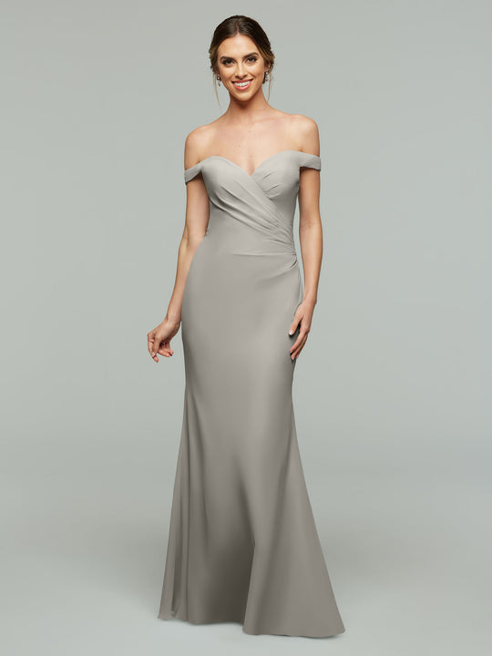 A woman smiles in an Avery Austin TH-80122 off-the-shoulder, floor-length fitted bridesmaid dress in silver chiffon, standing against a plain light gray background.