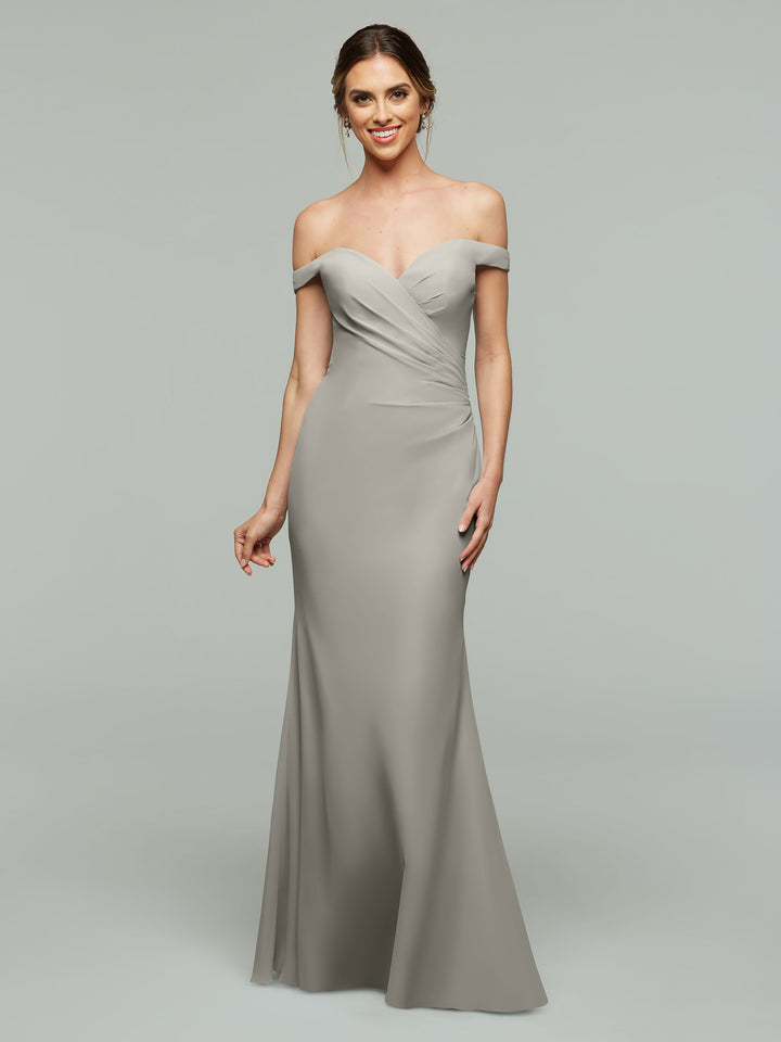 A woman smiles in an Avery Austin TH-80122 off-the-shoulder, floor-length fitted bridesmaid dress in silver chiffon, standing against a plain light gray background.