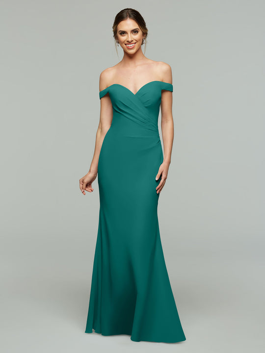 A woman smiles in the Avery Austin TH-80122 bridesmaid dress, a teal off-the-shoulder gown with a sweetheart neckline and slight ruching at the bodice, standing against a plain light gray background and wearing earrings.