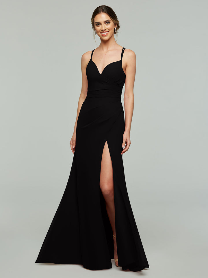 A woman wearing Avery Austin style 80130, a long black sleeveless sheath bridesmaid dress with thin straps and a thigh-high slit, smiles against a plain light gray background.