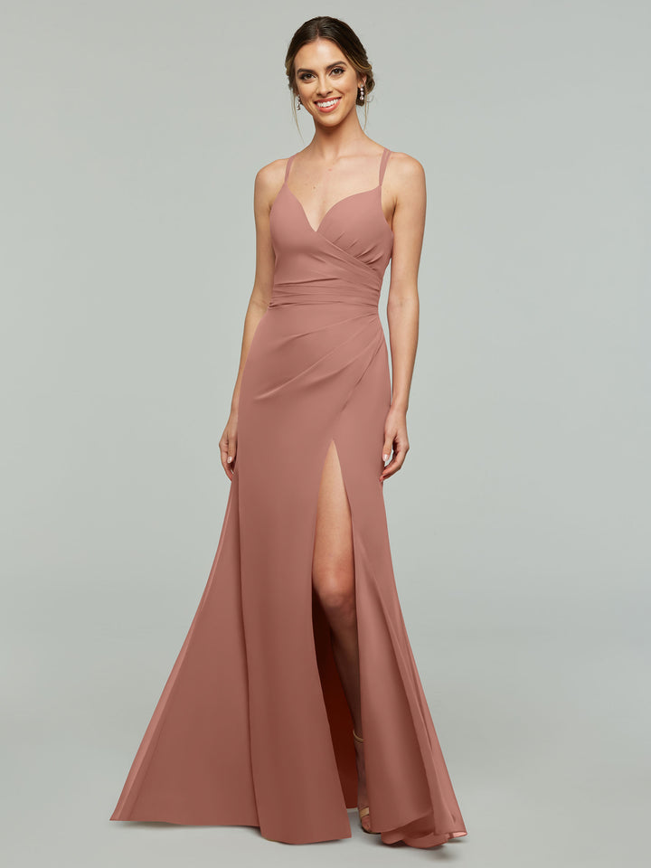 A woman wearing the Avery Austin 80130 sleeveless, floor-length rose chiffon bridesmaid dress with a v-neck, thigh-high slit, and fitted bodice stands against a plain light gray background.