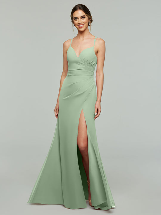 A woman wears the Avery Austin TH-80130 bridesmaid dress in Dusty Sage, featuring a v-neck, chiffon fabric, spaghetti straps, fitted bodice, and thigh-high slit, standing against a plain gray background.