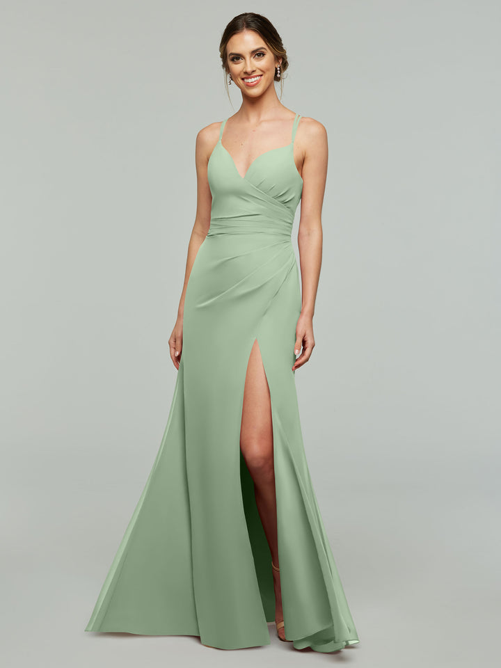 A woman wears the Avery Austin TH-80130 bridesmaid dress in Dusty Sage, featuring a v-neck, chiffon fabric, spaghetti straps, fitted bodice, and thigh-high slit, standing against a plain gray background.