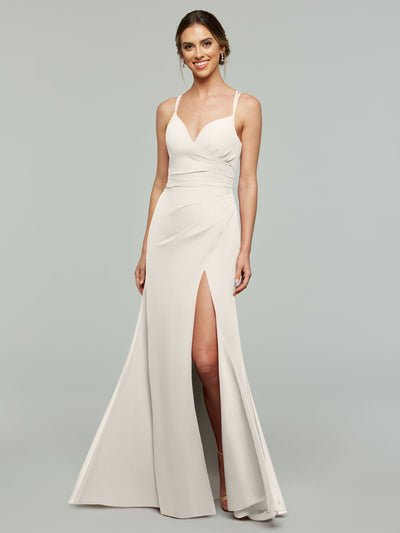 A woman models Avery Austin’s 80130, a sleeveless light beige sheath bridesmaid dress with a fitted bodice, V-neckline, and high thigh slit, standing against a plain light gray background and smiling.