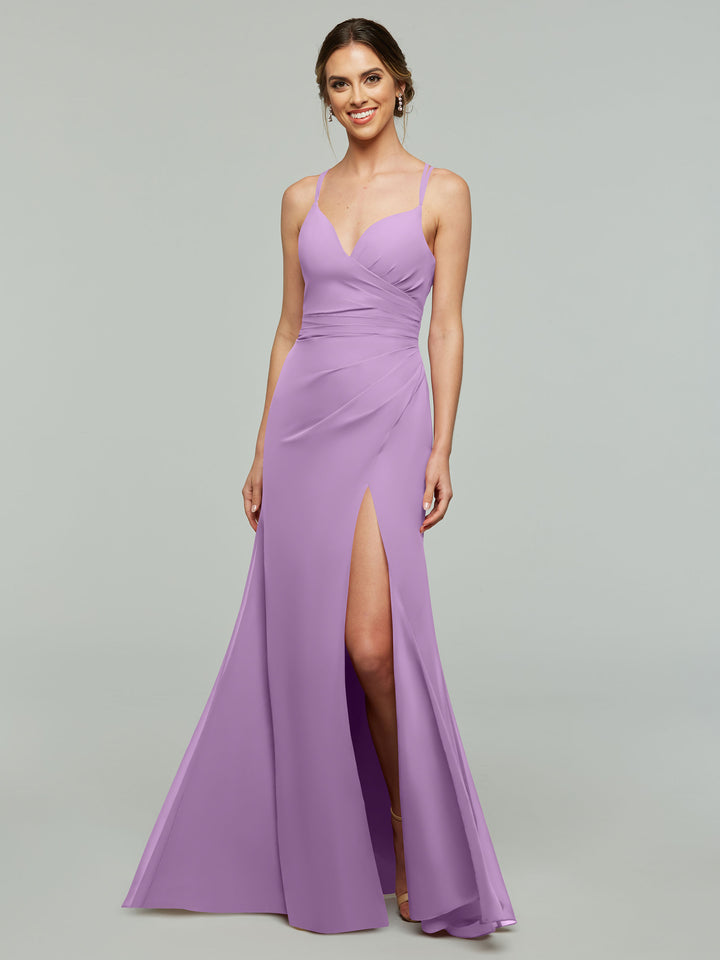 A woman smiles in Avery Austin’s 80130, a sleeveless floor-length lavender sheath bridesmaid dress with a thigh-high slit and ruched details, standing before a plain gray background.