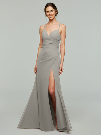 A woman stands against a plain light background wearing the Avery Austin 80130, a light gray floor-length sheath bridesmaid dress featuring thin straps, a wrapped bodice, and a high side slit.