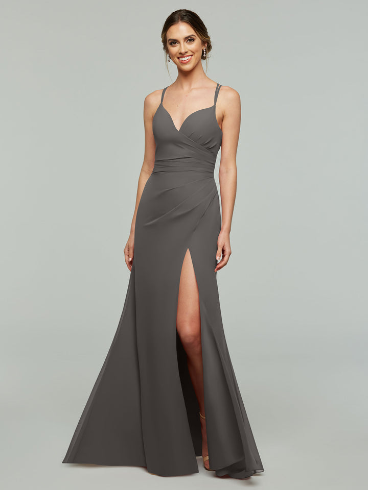 A woman in the Avery Austin 80130 sleeveless, floor-length charcoal gray sheath bridesmaid dress with a thigh-high slit and thin straps stands against a light gray background, smiling with her hair in a low updo.