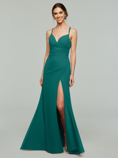 A woman stands and smiles against a light gray background, wearing Avery Austin's style 80130: a teal sheath bridesmaid dress with spaghetti straps, fitted bodice, and high thigh slit.