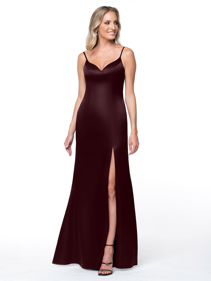 A woman models Avery Austin’s 80132, a sleeveless floor-length burgundy gown with thin straps, V-neckline, high side slit, and detailed back, standing against a white background.