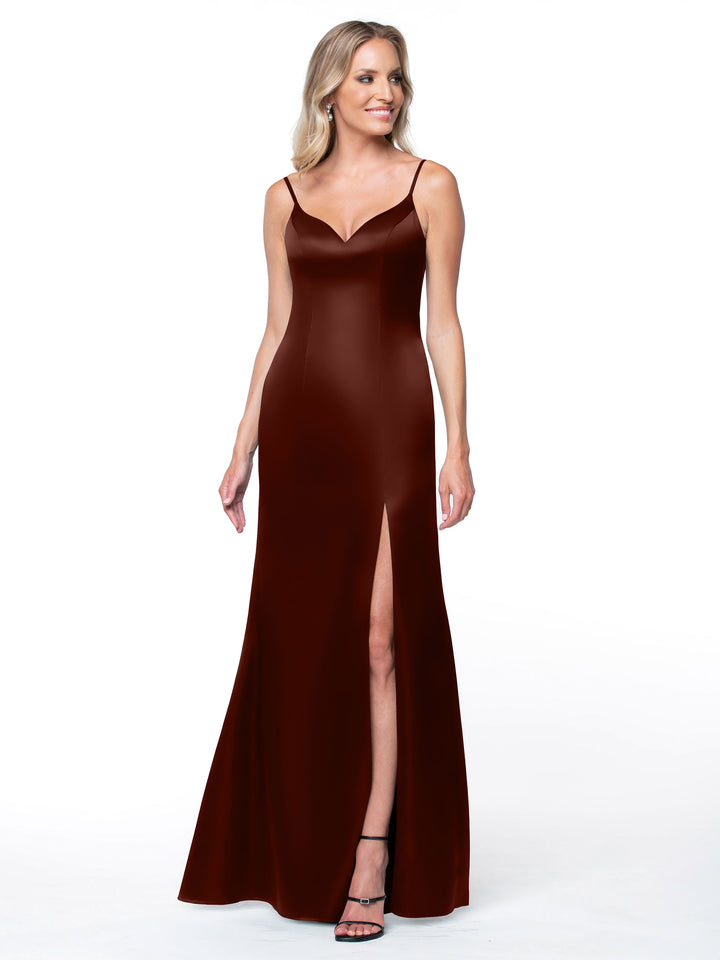 A woman wearing Avery Austin’s 80132—a sleeveless, floor-length dark red slit dress with thin straps and an intricate back—stands smiling against a plain white background.