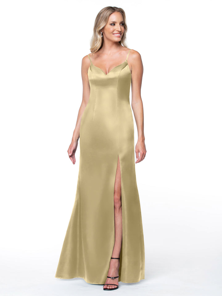 A woman models Avery Austin’s 80132: a gold, sleeveless floor-length slit dress. She steps forward against a white backdrop, smiling, with long wavy blonde hair and black strappy heels accenting the gown&