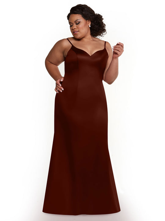 A woman poses confidently against a white background in the Avery Austin TH-80132 burgundy sleeveless, floor-length dress with thin straps and a side slit, one hand on her hip and the other raised slightly.