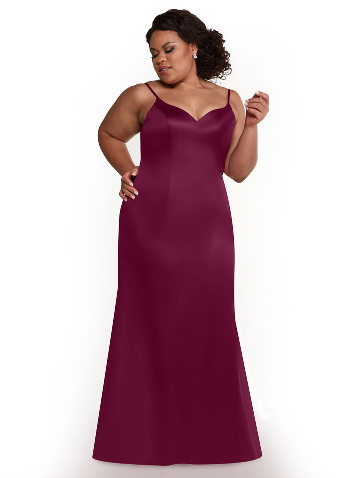 A woman with curly hair models Avery Austin’s floor-length, sleeveless fit and flare dress (style 80132) in dark magenta with a sweetheart neckline, set against a plain white background.