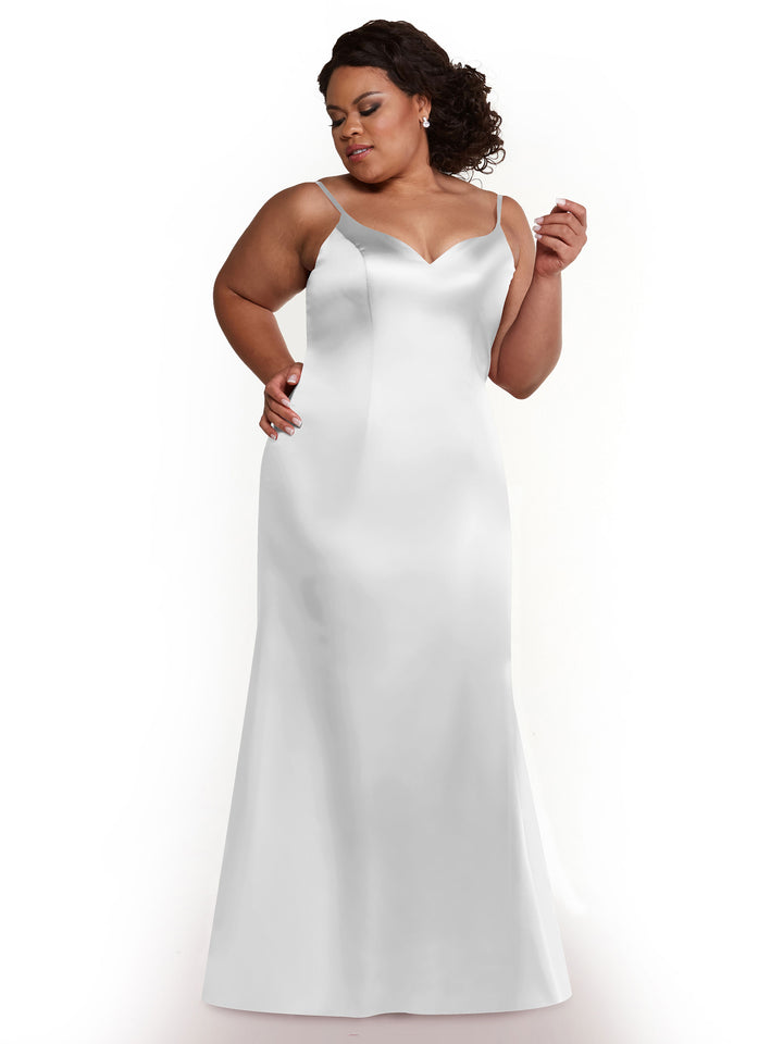 A woman models Avery Austin’s 80132, a sleeveless floor-length white satin slit dress with thin straps and an intricate back, standing against a plain white background while looking down and to the side with one hand on her hip.