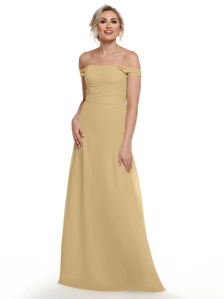 A woman stands and smiles against a plain white background, wearing the Avery Austin 80136 light beige, floor-length, off-the-shoulder chiffon dress with one hand by her side and the other on her hip.
