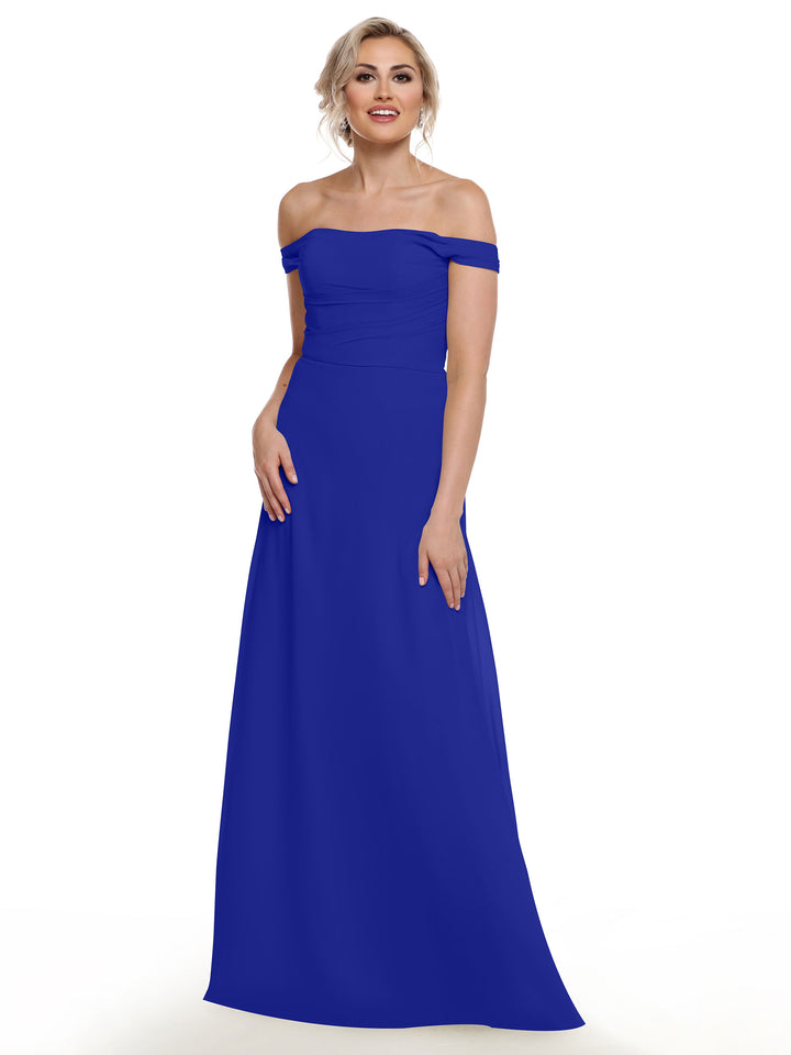 A woman stands and smiles against a white background wearing Avery Austin style 80136, a royal blue off-the-shoulder chiffon dress. Her hair is styled up and she displays a relaxed, confident posture.