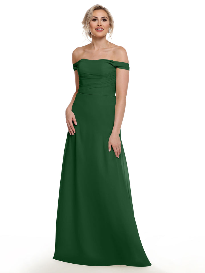 A woman models Avery Austin style 80136: a dark green, floor-length off-the-shoulder chiffon dress, standing against a white background and smiling with one hand at her side and the other resting on her hip.