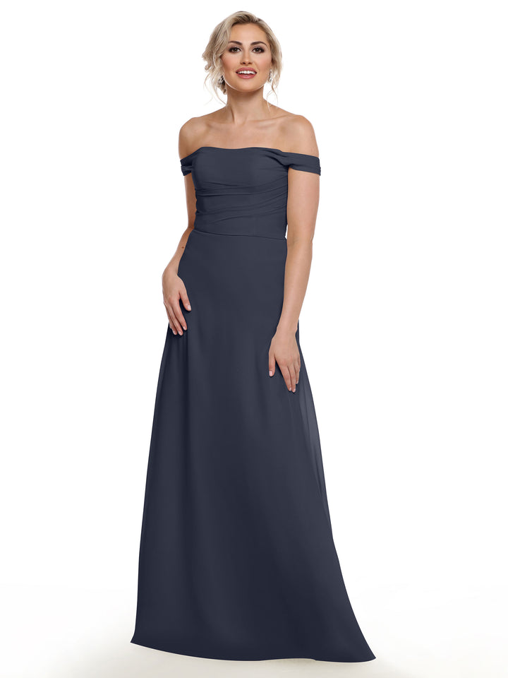 A woman smiles in Avery Austin’s 80136 dress—an off-the-shoulder, floor-length chiffon gown with a fitted bodice, short sleeves, and flowing skirt. She poses with her light hair styled up against a white background.