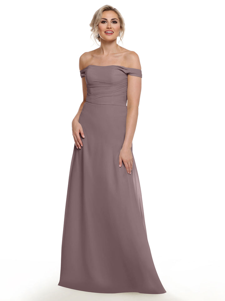 A woman in Avery Austin’s 80136, an off-the-shoulder mauve chiffon gown with a fitted bodice and flowing floor-length skirt, stands smiling against a plain white background.