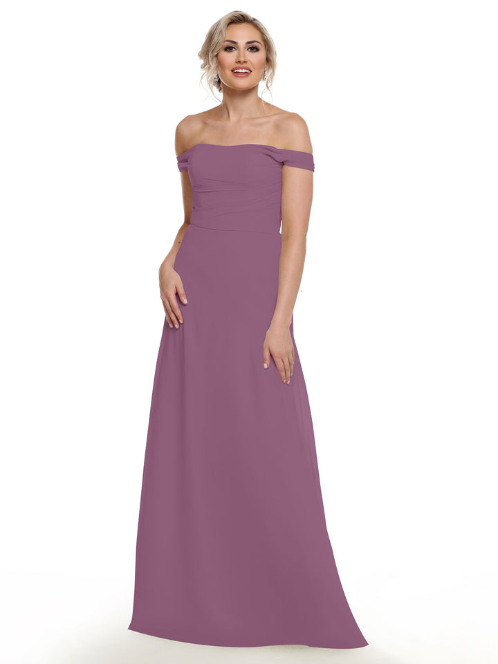 A woman with blonde hair in an updo is wearing the Avery Austin 80136 mauve off-the-shoulder chiffon gown. She stands smiling, one hand on her hip, against a white background.