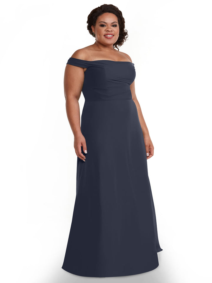 A woman wearing the Avery Austin 80136 off-the-shoulder, floor-length chiffon dress stands smiling against a plain white background.