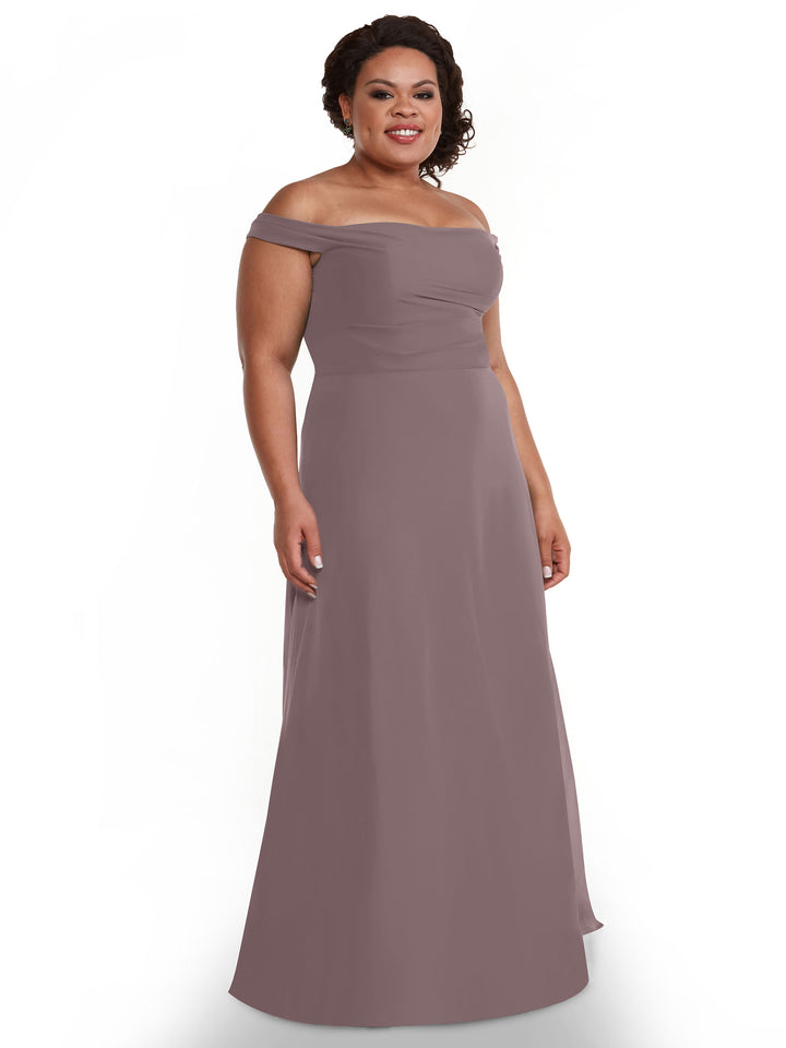 A woman smiles in front of a white background, wearing Avery Austin’s 80136: a mauve off-the-shoulder floor-length chiffon dress with a fitted bodice and A-line skirt.