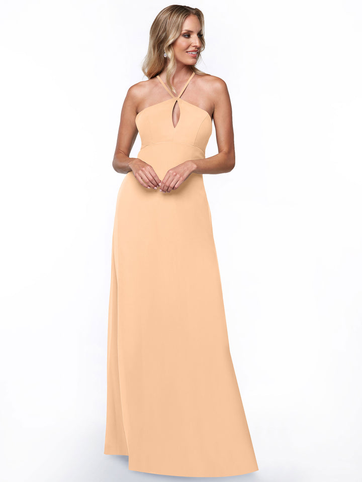 A woman smiles against a plain white background wearing Avery Austin’s 80137, a long peach sleeveless halter dress with a keyhole back.