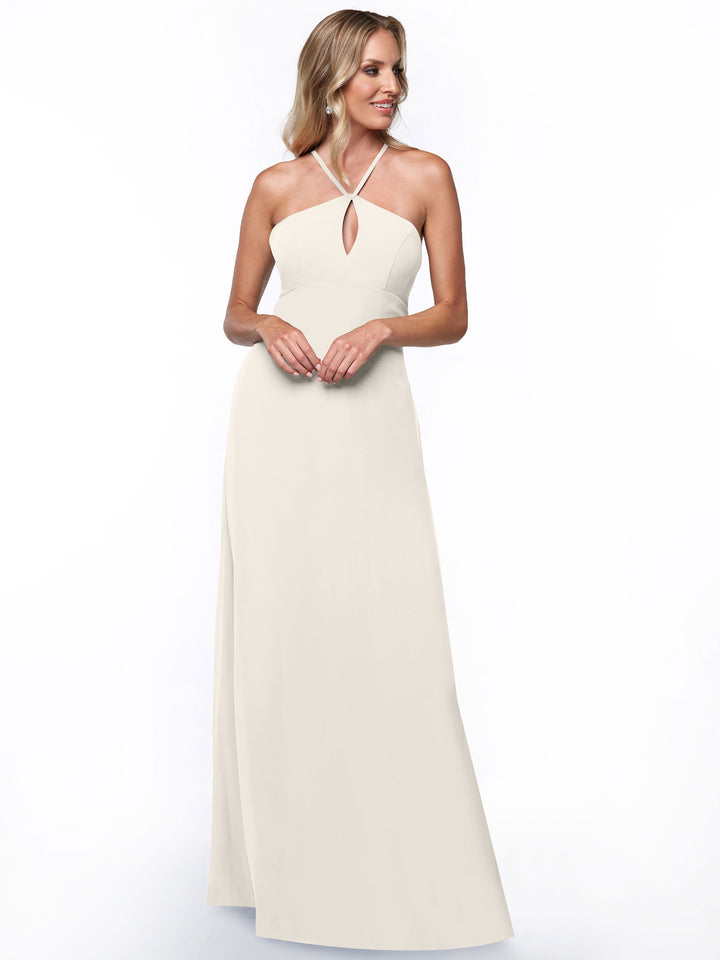 A woman in Avery Austin’s 80137—a minimalistic, sleeveless, floor-length light ivory halter dress with a keyhole back—stands smiling against a plain white background.