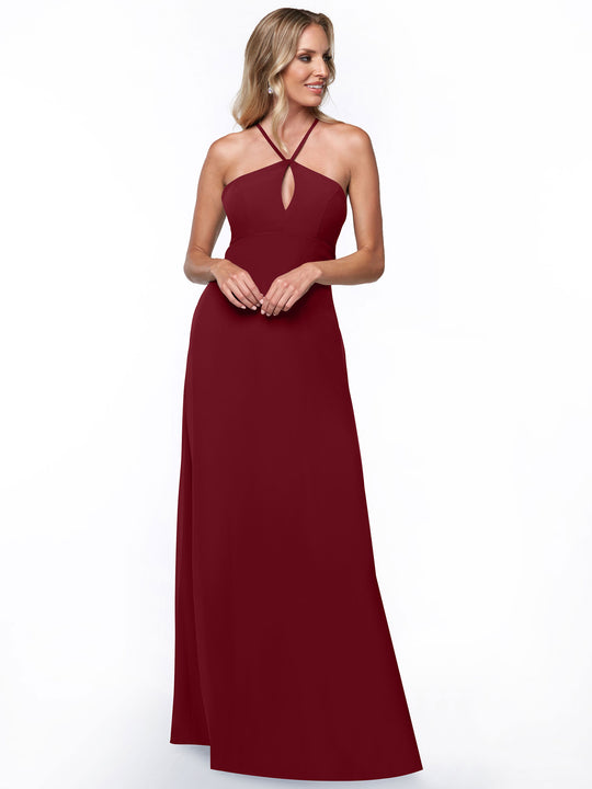 A woman wears Avery Austin’s 80137, a minimalistic burgundy halter dress with a keyhole cutout and floor-length design, standing against a white background and smiling as she looks to the side.