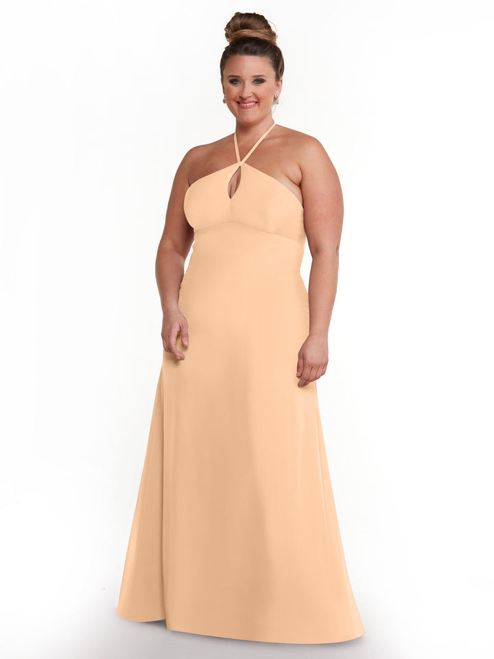 A woman smiles against a white background wearing Avery Austin’s 80137: a minimalistic peach halter dress with a keyhole neckline, paired with earrings and a neat bun.